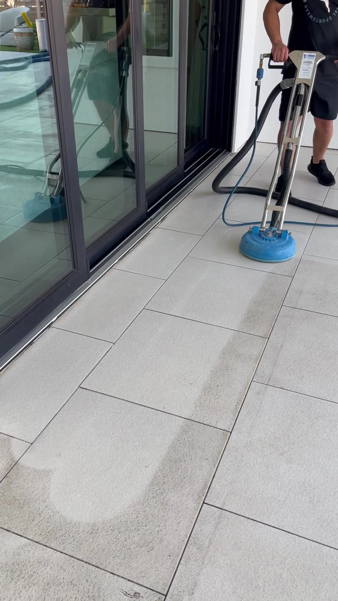 Technician cleaning patio tile beside sliding glass doors.